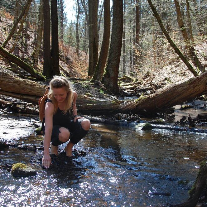 Wanderin hockt am Rand der Schlaube und fühlt das Wasser an ihren Fingern
