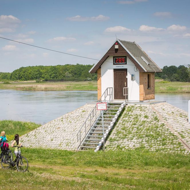 Radfahrer stehen an einem alten Pegelhäuschen an der Oder