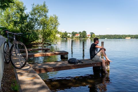Mann sitzt auf einem Steg und blickt auf einen See 