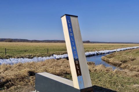 Eine Stele steht am Wegesrand in Winterlandschaft mit blick auf einen kleinen Fluss.