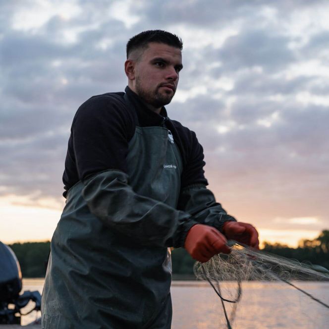 Fischer bei Sonnenaufgang auf dem Boot holt Netz ein