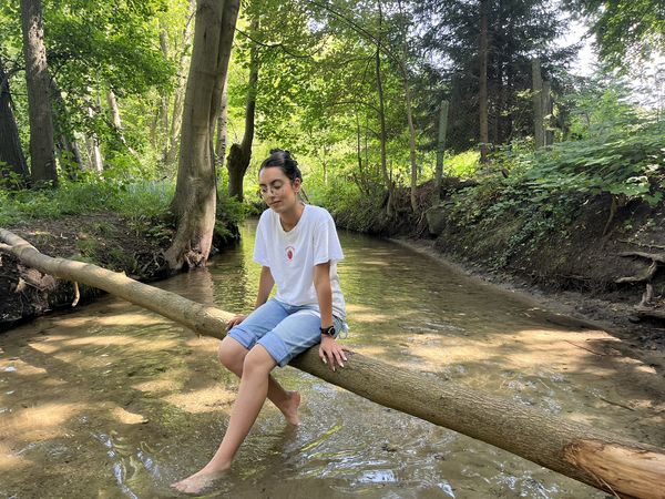 Frau sitzt auf einem Baumstamm und hält die Füße ins Wasser