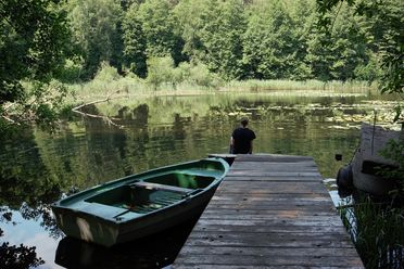 Ein Steg führt auf einen See, links vom Steg ist ein Ruderboot festgemacht.