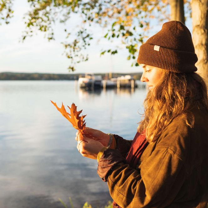 Frau hält ein orangenes Blatt in der Hand und steht an einem See