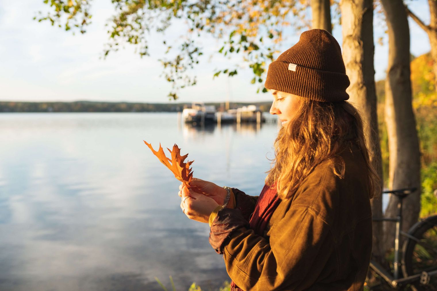 Frau hält ein orangenes Blatt in der Hand und steht an einem See