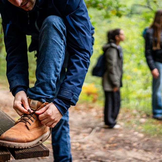 Wanderer beim Schuhe zubinden auf der Bank und 2 Wanderer im Hintergrund